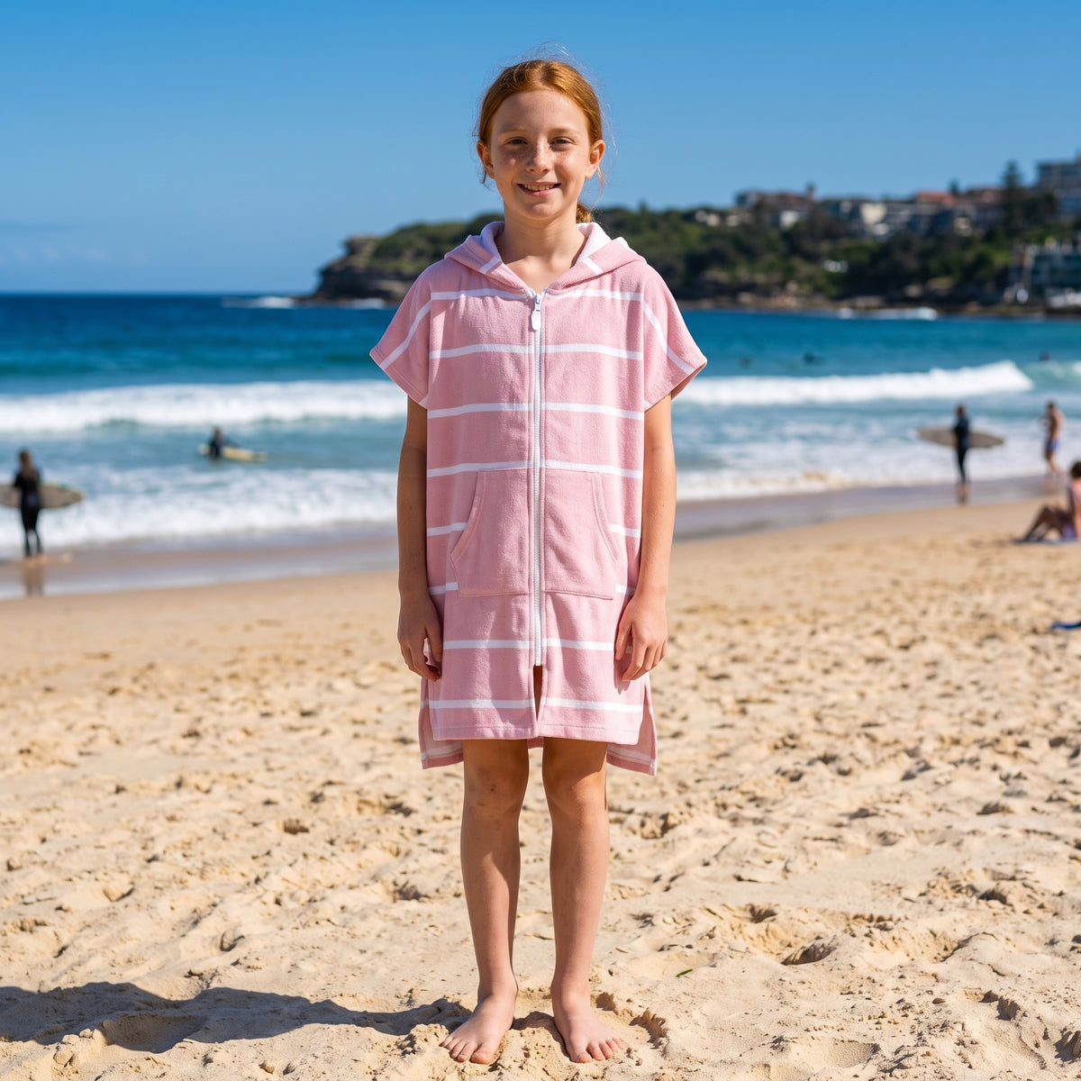 Girl wearing Amalfi pink and white striped kids hooded towel, on Bondi Beach, Sydney