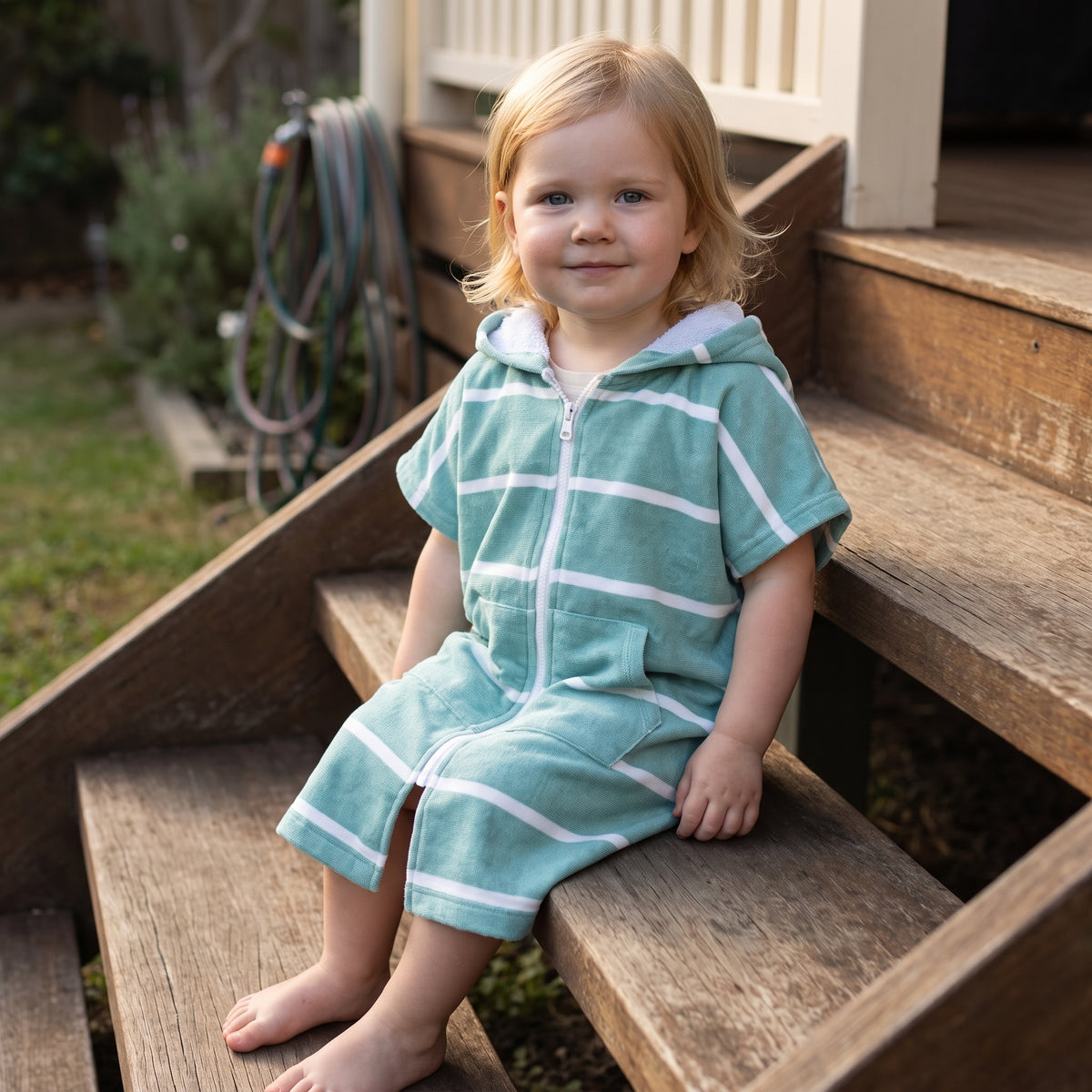 Toddler girl wearing Amalfi teal and white striped toddler hooded towel, on the back steps at home