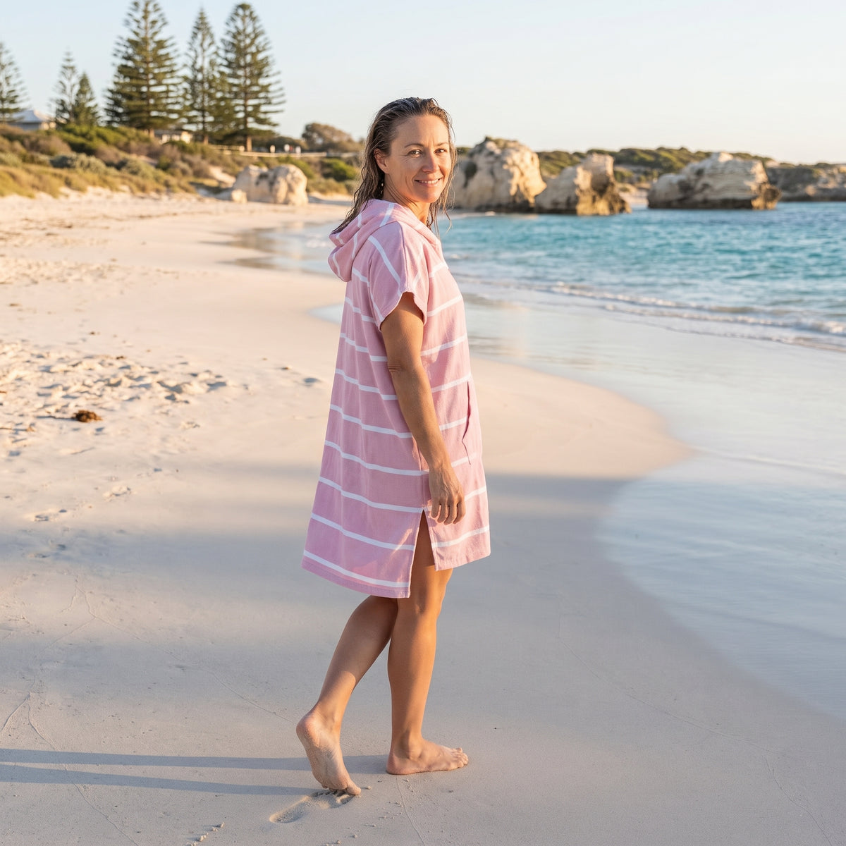 Woman wearing the Amalfi Pink White Turkish hooded towel while walking along a Western Australian beach