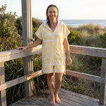 Woman wearing the Amalfi Yellow White Turkish hooded towel on a timber deck after swimming