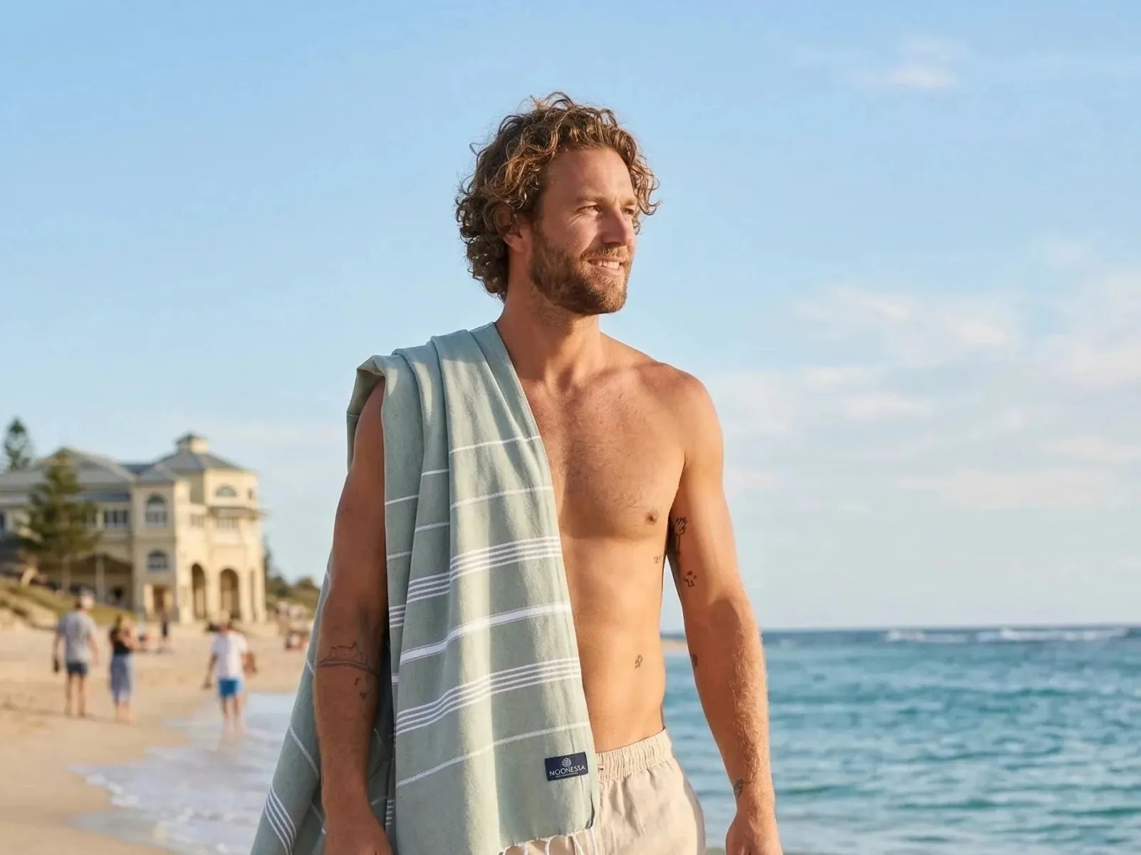 Man walking along Cottesloe Beach with the sand-free Buldan Turkish towel in khaki draped over his shoulder