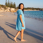 Woman wearing the Santorini Aqua hooded towel while walking along a Western Australian beach