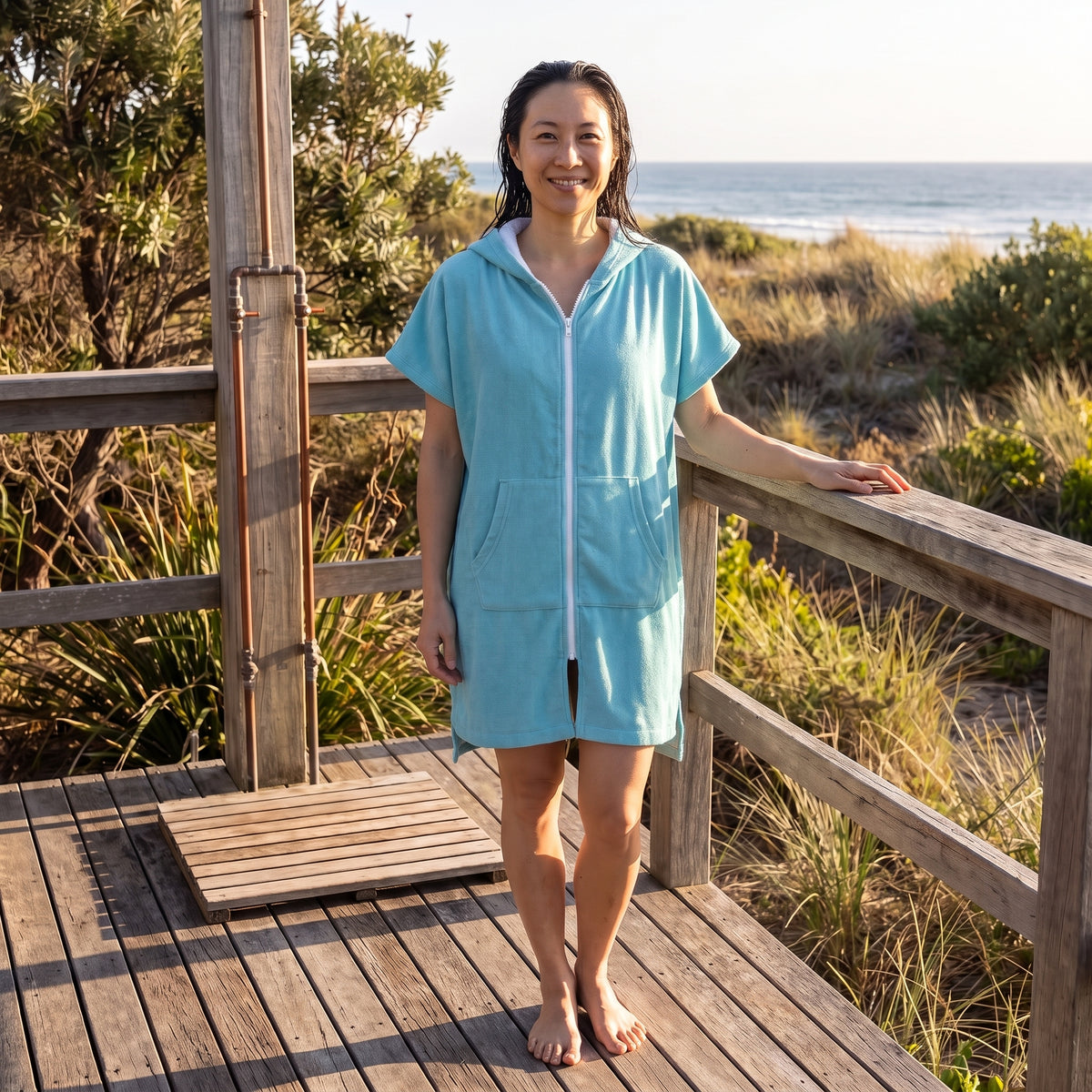 Woman wearing the Santorini Aqua hooded towel on a timber deck after swimming