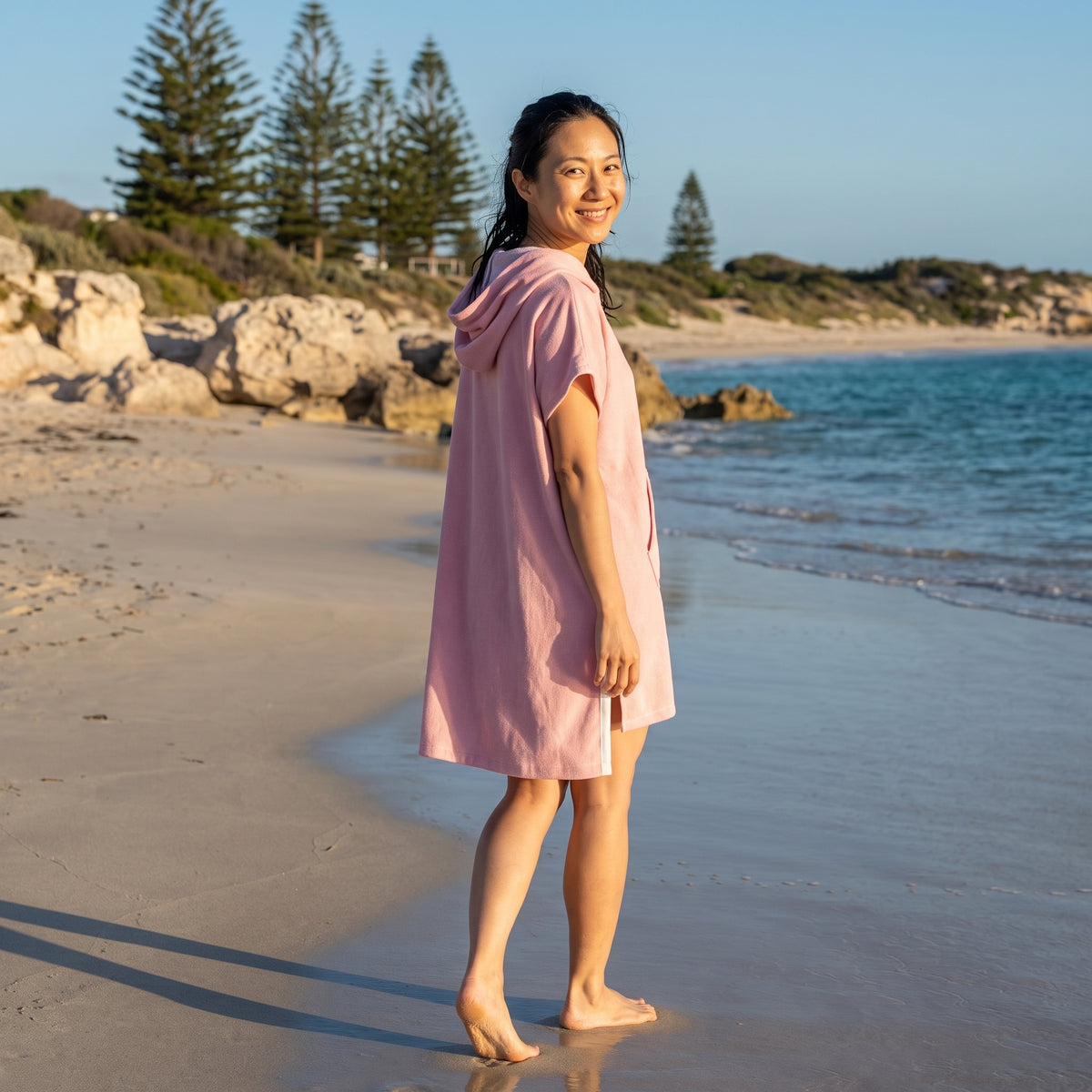 Woman wearing the Santorini Pink Turkish hooded towel while walking along a Western Australian beach