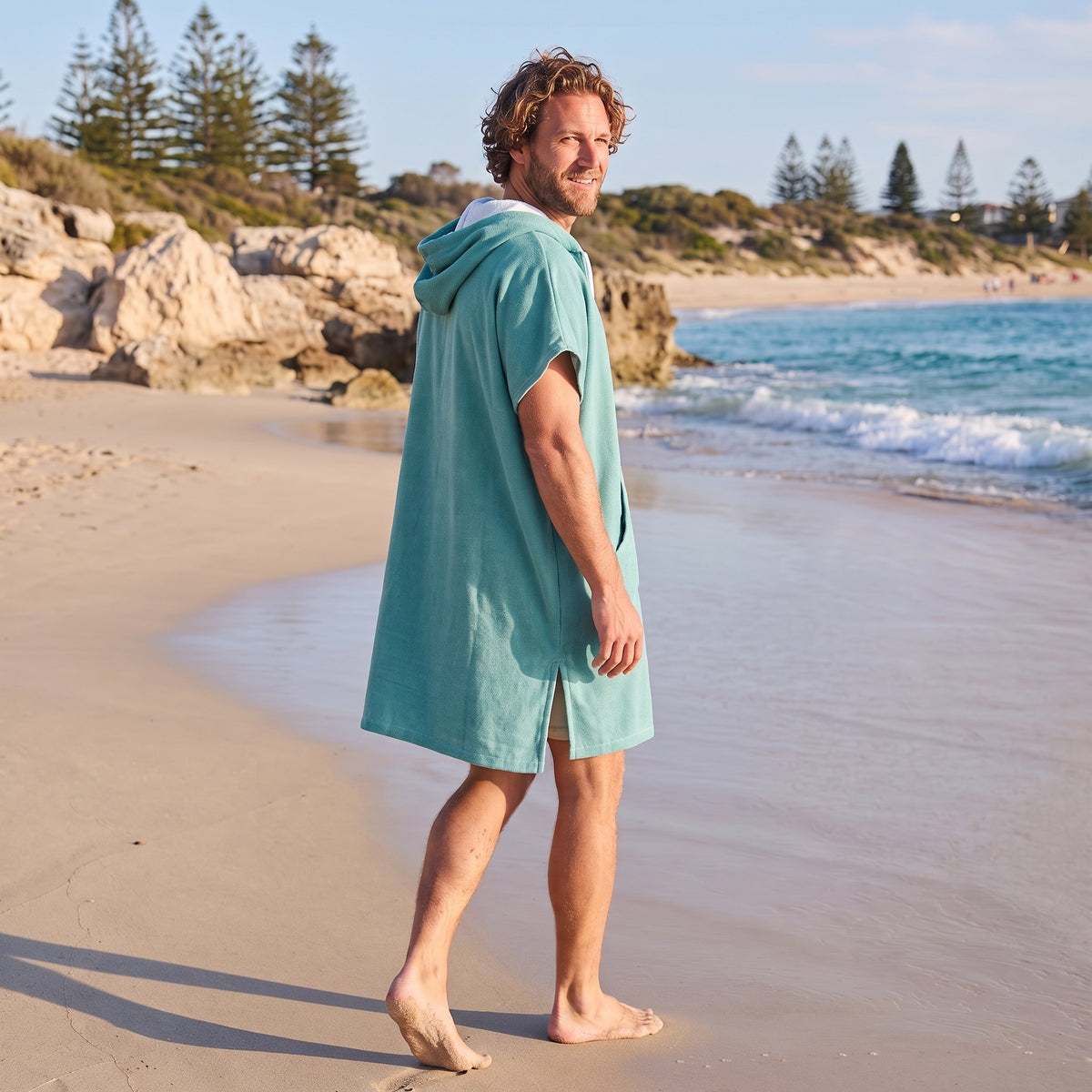 Man wearing the Santorini Teal hooded towel while walking along a Western Australian beach