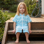 Young girl wearing Amalfi aqua and white striped kids hooded towel, on the back steps at home