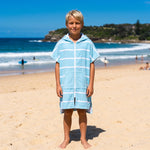 Amalfi kids hooded towel in aqua and white stripes worn by a boy, on Bondi Beach, Sydney