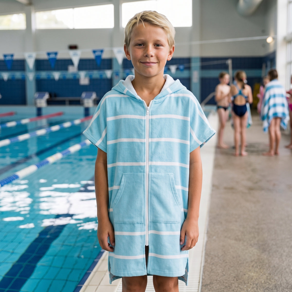 Boy in the Amalfi aqua and white kids zip hooded towel, after a swimming lesson at an indoor pool