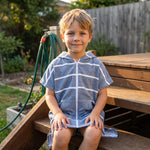Amalfi kids hooded towel in navy and white stripes worn by a young boy, on the back steps at home