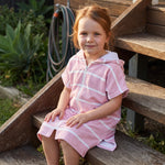 Amalfi kids hooded towel in pink and white stripes worn by a young girl, on the back steps at home