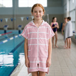 Girl in the Amalfi pink and white kids zip hooded towel, after a swimming lesson at an indoor pool