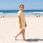 Girl in the Amalfi yellow and white kids zip hooded towel, walking on bright dry beach sand