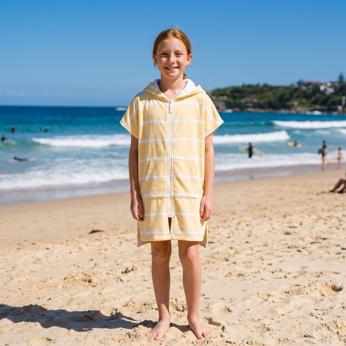 Girl wearing Amalfi yellow and white striped kids hooded towel, on Bondi Beach, Sydney