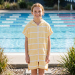 Girl wearing Amalfi yellow and white striped kids hooded towel, beside an outdoor pool