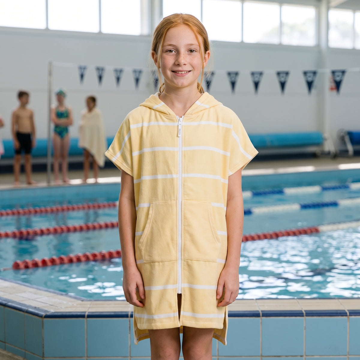 Amalfi kids hooded towel in yellow and white stripes worn by a girl, after a swimming lesson at an indoor pool