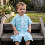 Toddler boy wearing Amalfi aqua and white striped toddler hooded towel, on the back steps at home