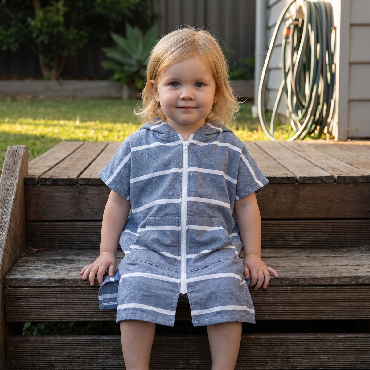 Amalfi toddler hooded towel in navy and white stripes worn by a toddler girl, on the back steps at home