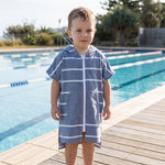 Toddler boy wearing Amalfi navy and white striped toddler hooded towel, beside an outdoor pool
