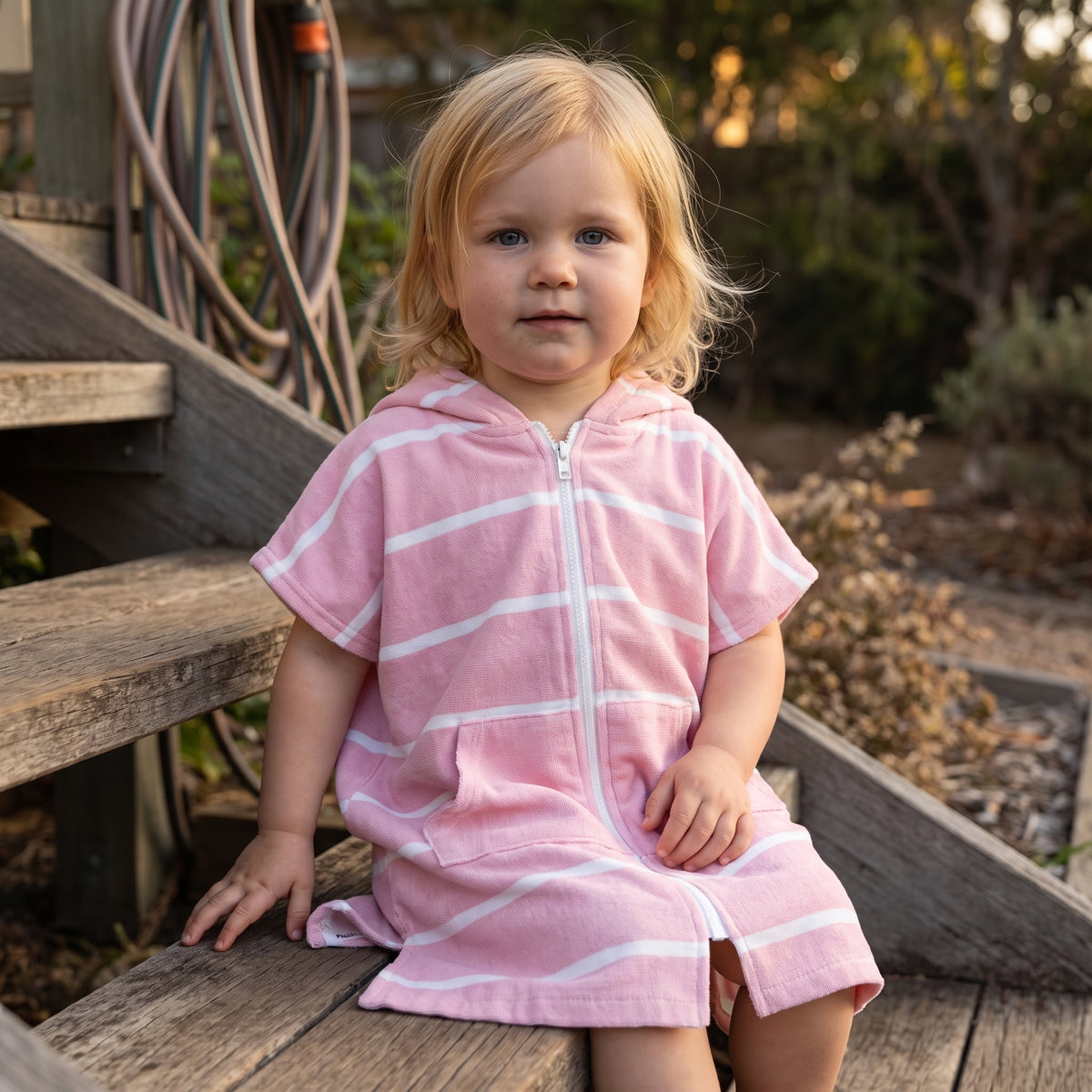 Toddler girl in the Amalfi pink and white toddler zip hooded towel, on the back steps at home