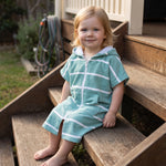 Toddler girl wearing Amalfi teal and white striped toddler hooded towel, on the back steps at home