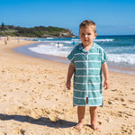 Amalfi toddler hooded towel in teal and white stripes worn by a toddler boy, on Bondi Beach, Sydney
