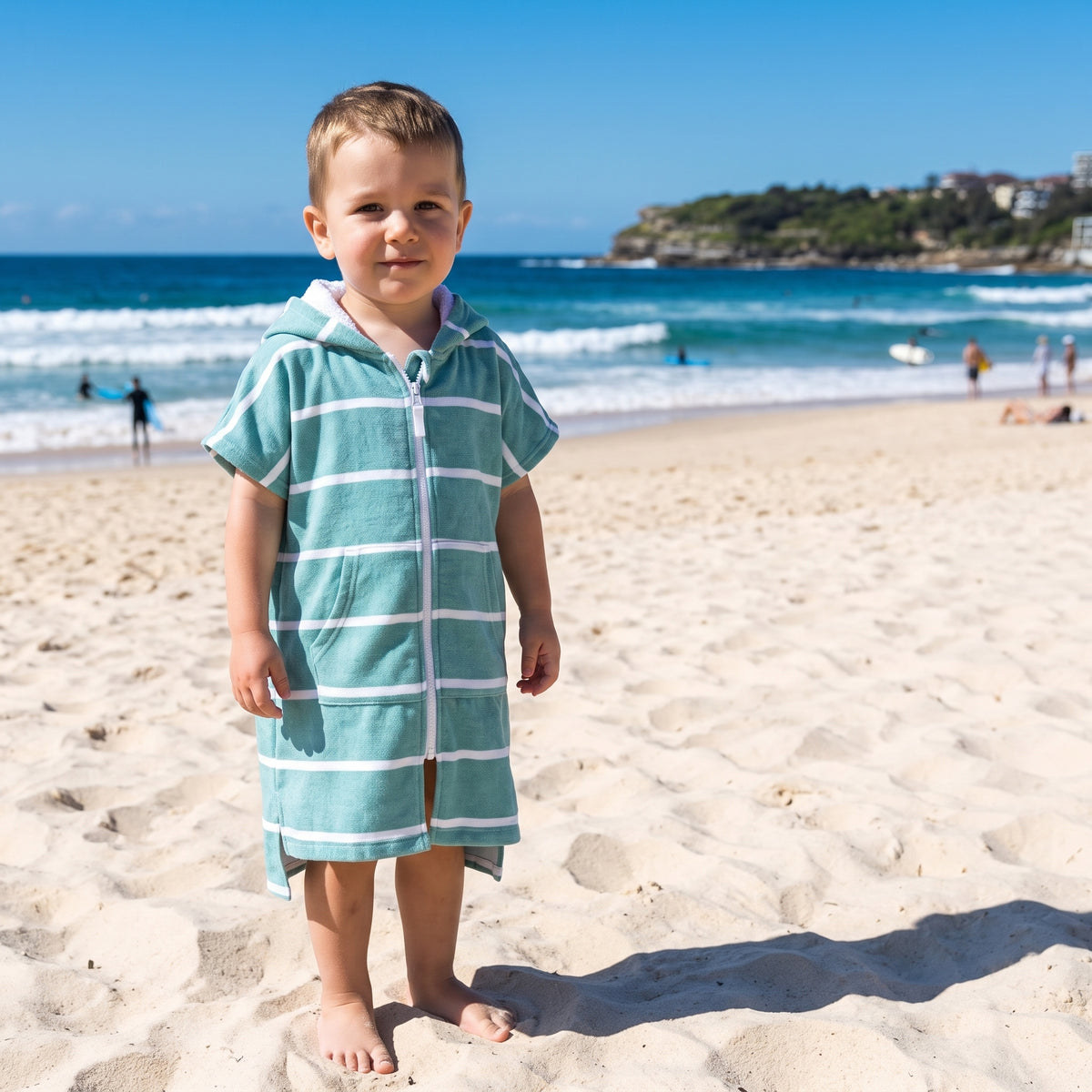 Amalfi toddler hooded towel in teal and white stripes worn by a toddler boy, on Bondi Beach, Sydney