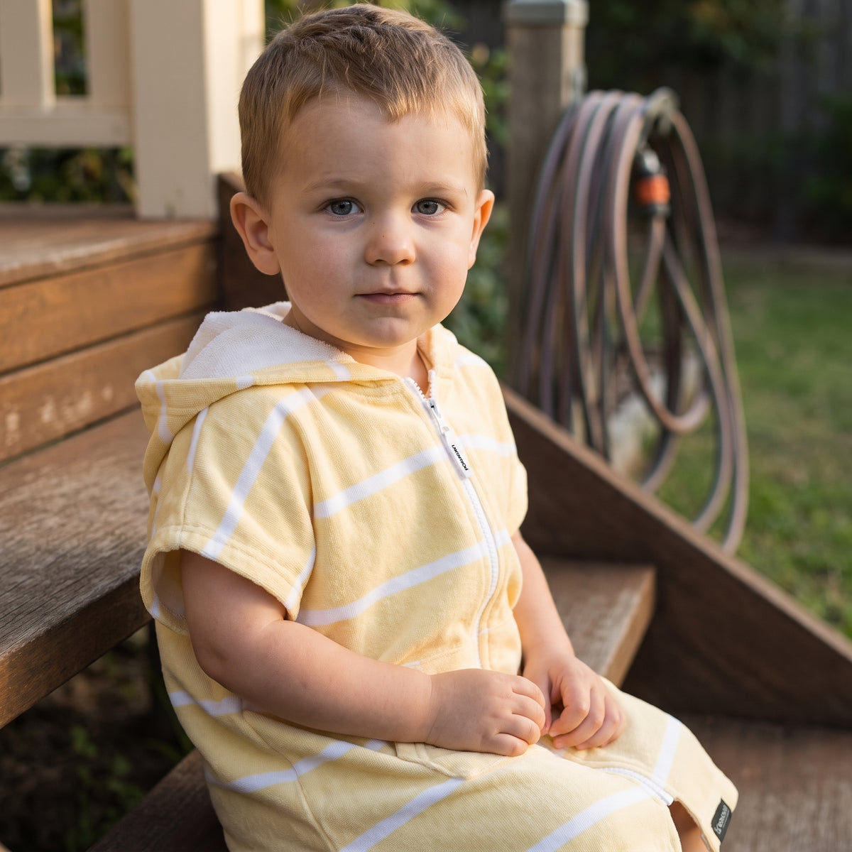 Toddler boy in the Amalfi yellow and white toddler zip hooded towel, on the back steps at home