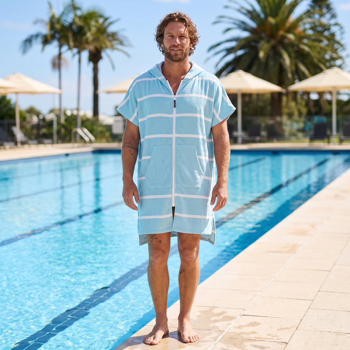 Man wearing the Amalfi Aqua White Turkish hooded towel beside an outdoor swimming pool