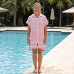 Woman wearing the Amalfi Pink White Turkish hooded towel beside an outdoor swimming pool