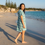 Woman wearing the Amalfi Teal White Turkish hooded towel while walking along a Western Australian beach