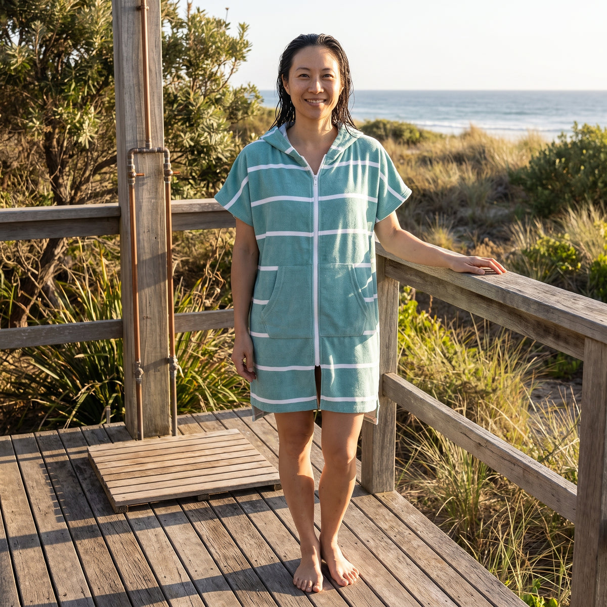Woman wearing the Amalfi Teal White Turkish hooded towel on a timber deck after swimming