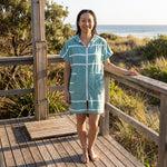 Woman wearing the Amalfi Teal White Turkish hooded towel on a timber deck after swimming