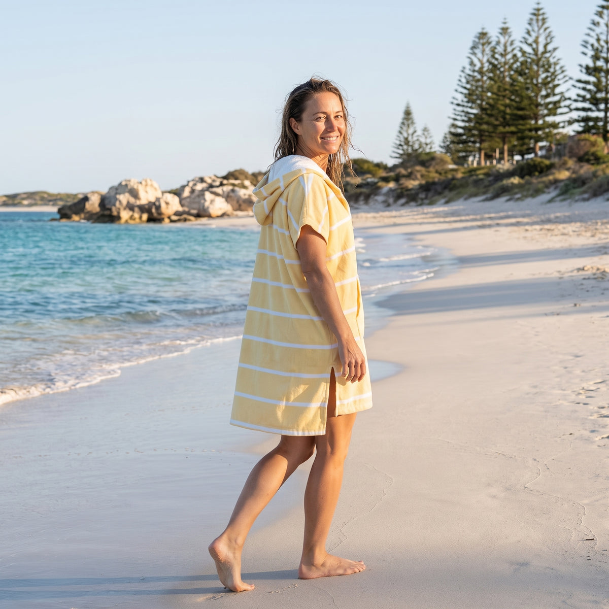 Woman wearing the Amalfi Yellow White Turkish hooded towel while walking along a Western Australian beach