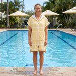 Woman wearing the Amalfi Yellow White Turkish hooded towel beside an outdoor swimming pool