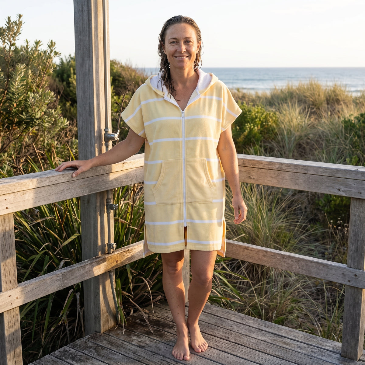 Woman wearing the Amalfi Yellow White Turkish hooded towel on a timber deck after swimming