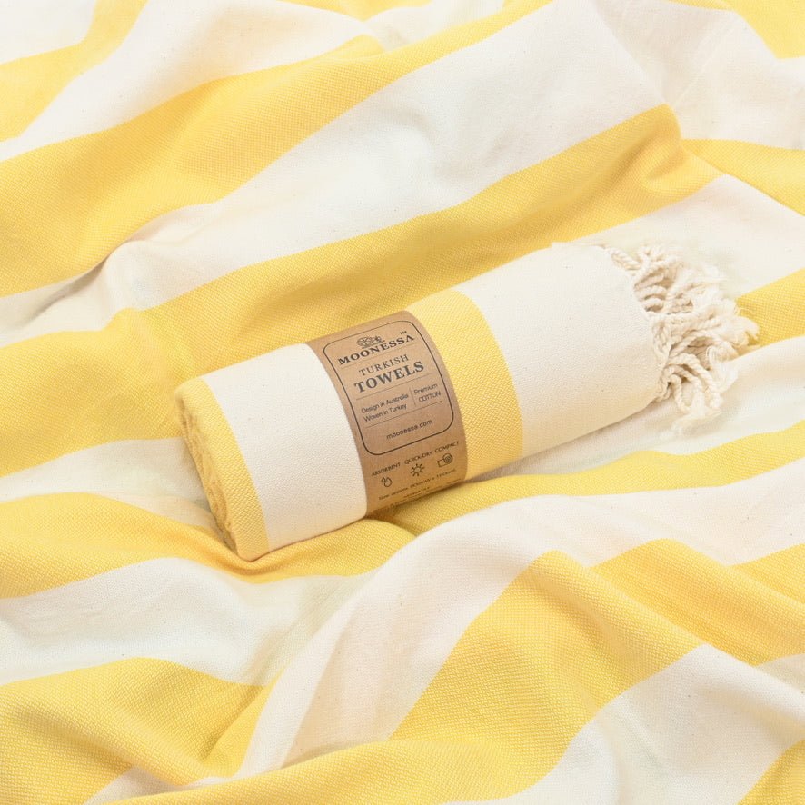 Avalon Turkish towel rolled in ecru and yellow, resting on its flat-woven spread