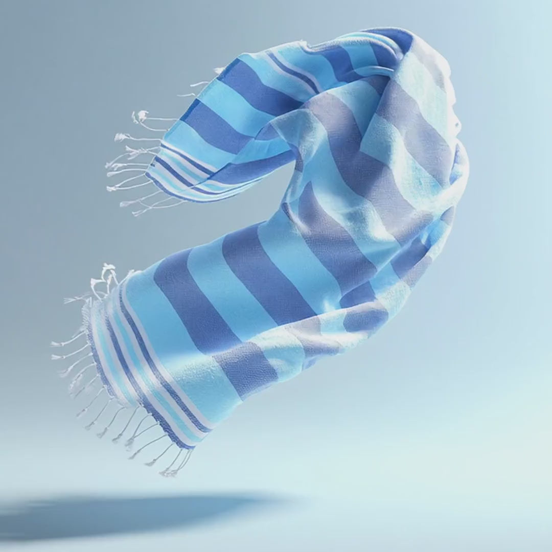 Moonessa Turkish towel unfurling in slow motion against a soft blue studio background