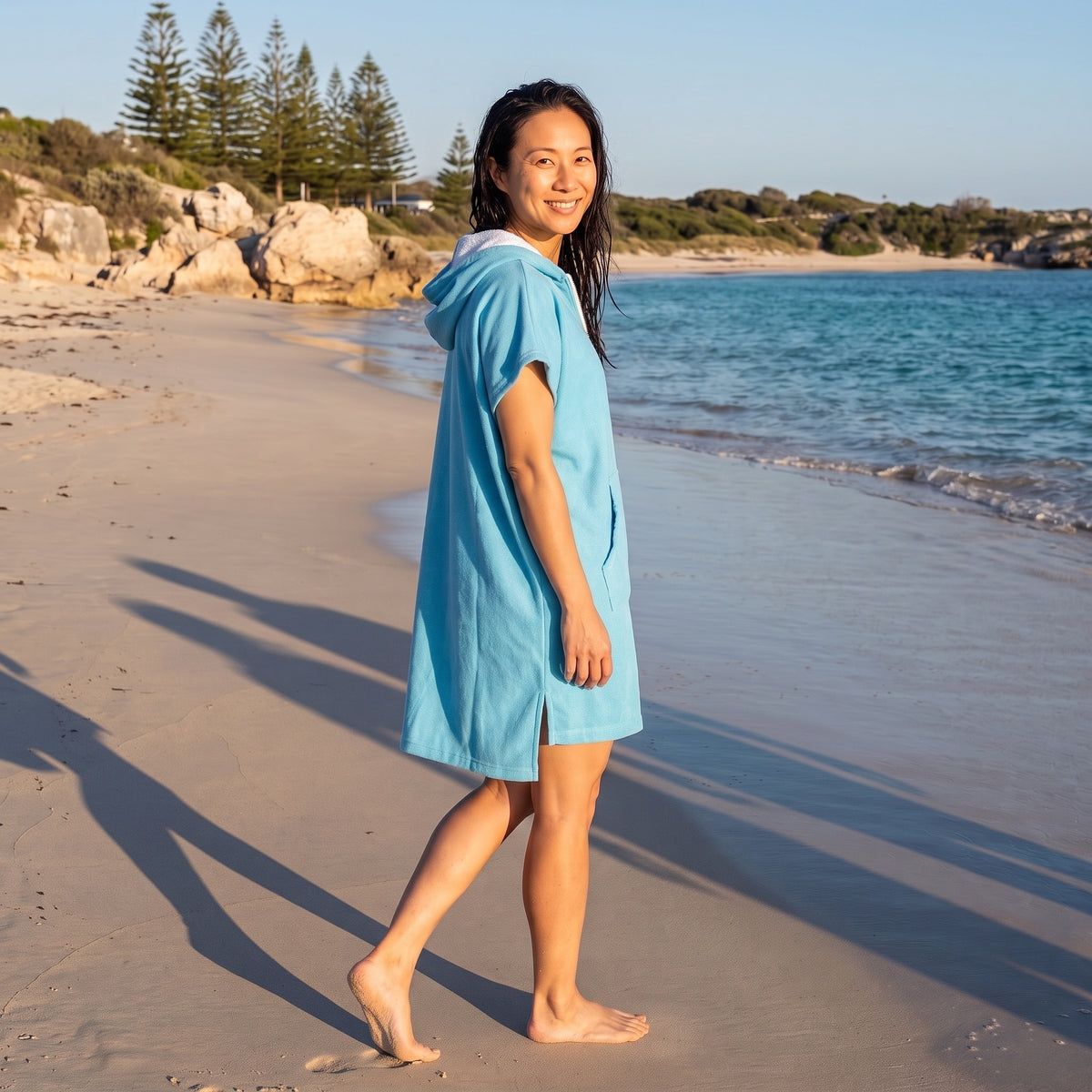 Woman wearing the Santorini Aqua hooded towel while walking along a Western Australian beach