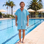 Man wearing the Santorini Aqua hooded towel beside an outdoor swimming pool