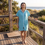 Woman wearing the Santorini Aqua hooded towel on a timber deck after swimming