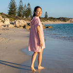Woman wearing the Santorini Pink Turkish hooded towel while walking along a Western Australian beach