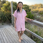 Woman wearing the Santorini Pink Turkish hooded towel on a timber deck after swimming