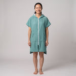 Woman wearing the Santorini Teal hooded towel, front view on a plain studio background