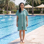 Woman wearing the Santorini Teal hooded towel beside an outdoor swimming pool